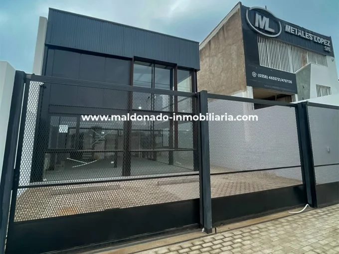Fachada y acceso al galpón en alquiler sobre Colectora A005, Río Cuarto, con frente vidriado y cerramiento metálico.